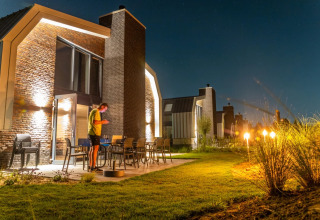 Cabaña moderna de glamping en un parque vacacional, iluminada de noche con persona en la terraza.