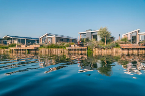 Foto von modernen Glamping-Unterkünften am Wasser in einem Ferienpark mit Spiegelung im ruhigen See.