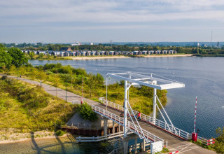 Blick auf eine Brücke am See mit modernen Glamping-Unterkünften im Hintergrund eines Ferienparks.