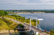 View of a bridge and scenic lake with modern glamping cabins in the background at a holiday park.