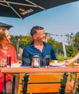 Pareja disfrutando de comida y bebida en una terraza soleada de un parque vacacional con camarera.