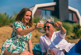 Paar genießt Wein vor einem Glamping-Haus im Ferienpark, sonniges Wetter und entspannte Atmosphäre.