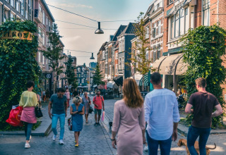 People walk along a lively street lined with shops and cafes at a holiday park with glamping options.