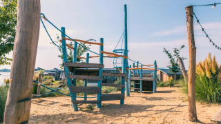 Parque infantil en arena con estructura para escalar en camping de lujo con cabañas y naturaleza.