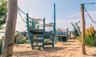 Parque infantil en arena con estructura para escalar en camping de lujo con cabañas y naturaleza.