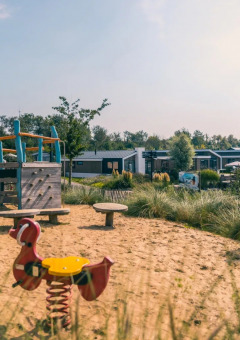 Spielplatz mit Sand und Klettergerüst, moderne Glamping-Unterkünfte im Hintergrund in einem Ferienpark.