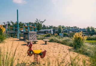 Legeplads med sand, legeredskaber og moderne glamping-hytter i baggrunden i en feriepark.