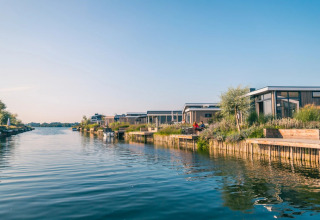 Holiday park with modern glamping cabins by the water, featuring a clear blue sky on a summer day.
