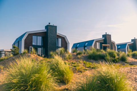 Foto de cabañas modernas en un parque vacacional entre dunas y pastos, ideales para glamping junto al mar.