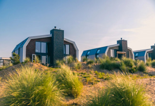 Foto de cabañas modernas en un parque vacacional entre dunas y pastos, ideales para glamping junto al mar.