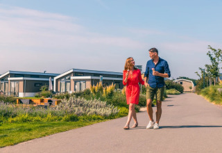 Ein Paar genießt Eis und spaziert auf einem Weg zwischen modernen Glamping-Unterkünften im Ferienpark.