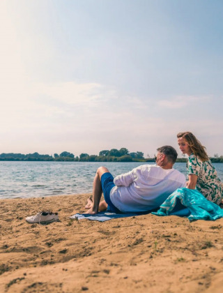 Una pareja descansa en la playa de un lago en un parque vacacional que ofrece alojamiento de glamping.