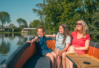 Een lachende vrouw en twee meisjes genieten samen op een bootje bij een vakantiepark met glamping.