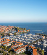 Luftaufnahme eines Ferienparks am Wasser mit Jachthafen, roten Dächern und Glamping-Unterkünften.