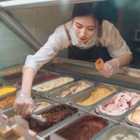 Trabajadora de heladería sirve helado en un cucurucho tras el mostrador en un parque de glamping vacacional.