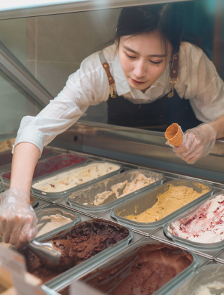 Trabajadora de heladería sirve helado en un cucurucho tras el mostrador en un parque de glamping vacacional.