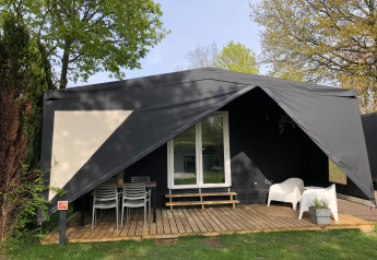 Zwarte safaritent Coco Deluxe met overdekt terras, tuinstoelen en groene bomen in de omgeving.