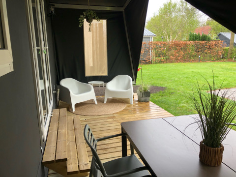 Terrasse couverte devant la tente safari Coco Deluxe au Vakantiepark Delftse Hout, avec sièges modernes.