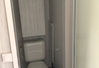 Et lille badeværelse i en safari-telt hytte med toilet, cisterne og el-skab i Vakantiepark Delftse Hout.