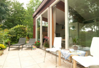 Udendørs terrasse med liggestole og stole ved Grasdakbungalow, Vakantiepark Delftse Hout, Holland.