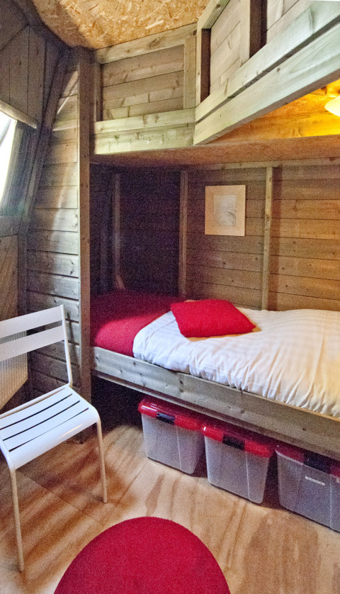 Intérieur d'une tiny house en bois au Holiday Park Delftse Hout avec lit, chaise et boîtes de rangement.