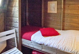 Indvendigt billede af et hyggeligt trætinyhouse med enkeltseng, stol og opbevaringskasser i Delftse Hout.