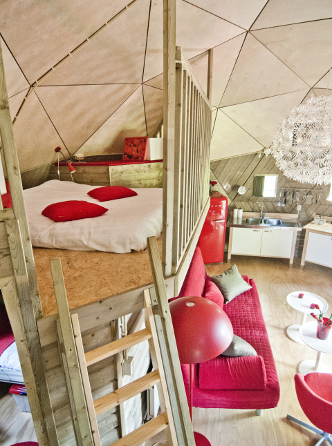 Intérieur du Wooden Igloo au Holiday Park Delftse Hout, Pays-Bas, avec canapé rouge et lit mezzanine.