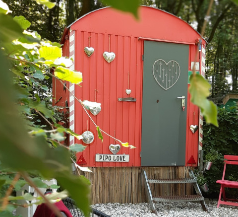 Lille rød tiny house ved navn Pipo Love, dekoreret med sølvhjerter, i grøn skov baggrund.