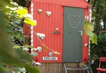 Lille rød tiny house ved navn Pipo Love, dekoreret med sølvhjerter, i grøn skov baggrund.