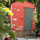 Lille rød tiny house ved navn Pipo Love, dekoreret med sølvhjerter, i grøn skov baggrund.