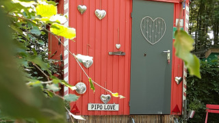 Kleine rote Tiny-House-Hütte namens Pipo Love, verziert mit silbernen Herzen, im Wald.
