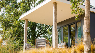 Moderne strandlodge bij Vakantiepark Leukermeer met terras en zetels, omgeven door natuur en bomen.