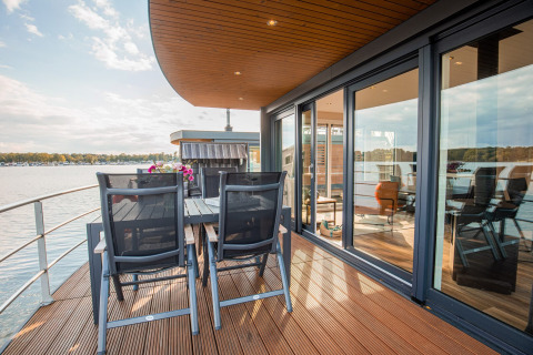 Casa flotante con terraza y comedor junto al agua en Vakantiepark Leukermeer, Países Bajos, en un día soleado.