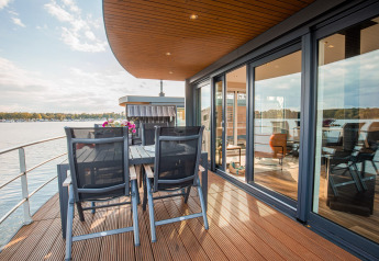 Casa flotante con terraza y comedor junto al agua en Vakantiepark Leukermeer, Países Bajos, en un día soleado.
