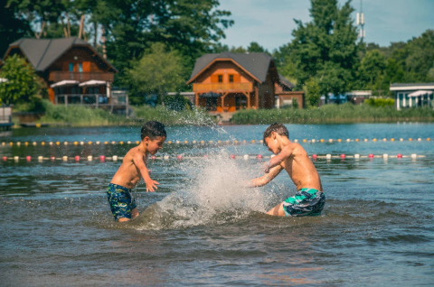 Twee jongens spelen en spetteren in het water bij een vakantiepark met glamping en houten huisjes.