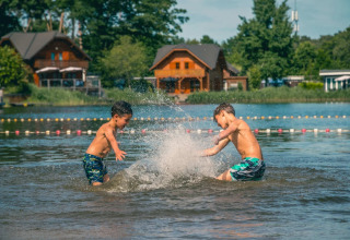 Twee jongens spelen en spetteren in het water bij een vakantiepark met glamping en houten huisjes.