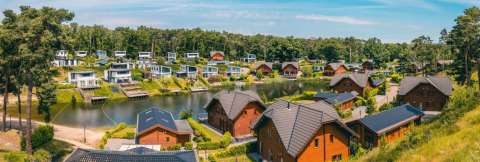 Panoramisch uitzicht op een vakantiedomein met glampinghuizen rond een meer in een bosrijke omgeving.