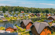 Panoramisch uitzicht op een vakantiedomein met glampinghuizen rond een meer in een bosrijke omgeving.