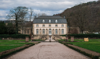 Elegante mansión cerca de Utscheid, Alemania, rodeada de jardines bien cuidados, árboles y colinas al fondo.