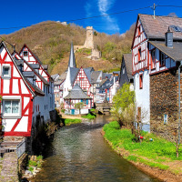 Vista pintoresca de un pueblo alemán con casas entramadas, un arroyo y una ruina de castillo en una colina.