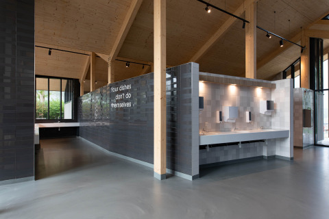Modern communal dishwashing area at Vakantiepark Delftse Hout, Netherlands, with a playful wall message.
