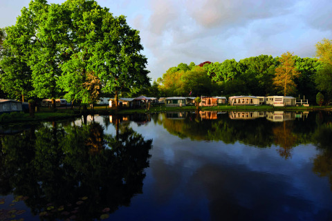 Reflejo de caravanas y árboles frondosos junto al lago en Camping Batenstein, Utrecht, Países Bajos.