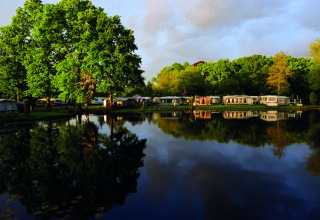 Reflection of caravans and lush green trees by a lake at Camping Batenstein, Utrecht, Netherlands.