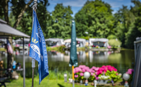 Bandera azul con pez y corona en un camping junto a un lago, flores y árboles en Utrecht, Países Bajos.