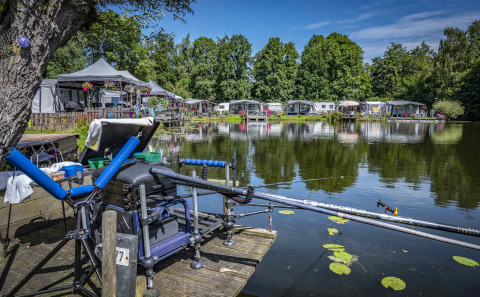 Camping Batenstein en Utrecht, Países Bajos, caña de pescar junto al lago y caravanas al fondo.