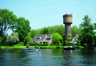 Bootjes varen op een rivier nabij Woerden, Nederland, met een oude watertoren en huizen tussen het groen.