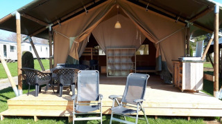 Safari tent at Camping Oos Heem in Belgium, featuring a wooden deck, chairs, and outdoor dining area.