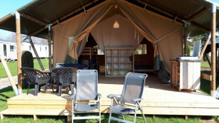 Safaritent op Camping Oos Heem in België met houten terras, tuinstoelen en buitentafel.