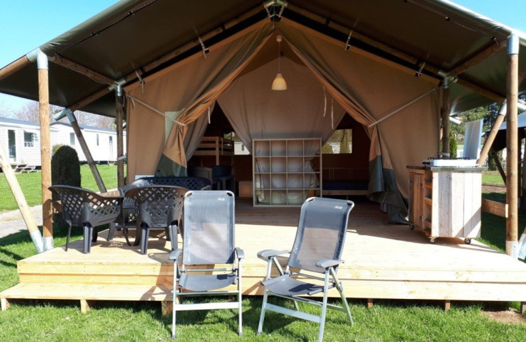Safaritent bij Camping Oos Heem in België met houten terras, stoelen en buiteneetgedeelte.