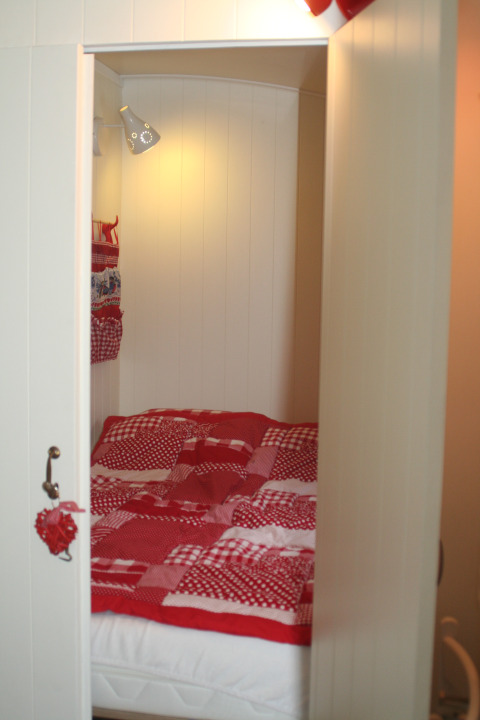 Gemütliche Schlafkoje mit roter Patchwork-Decke in Pipowagen im Camping De Grienduil in den Niederlanden.